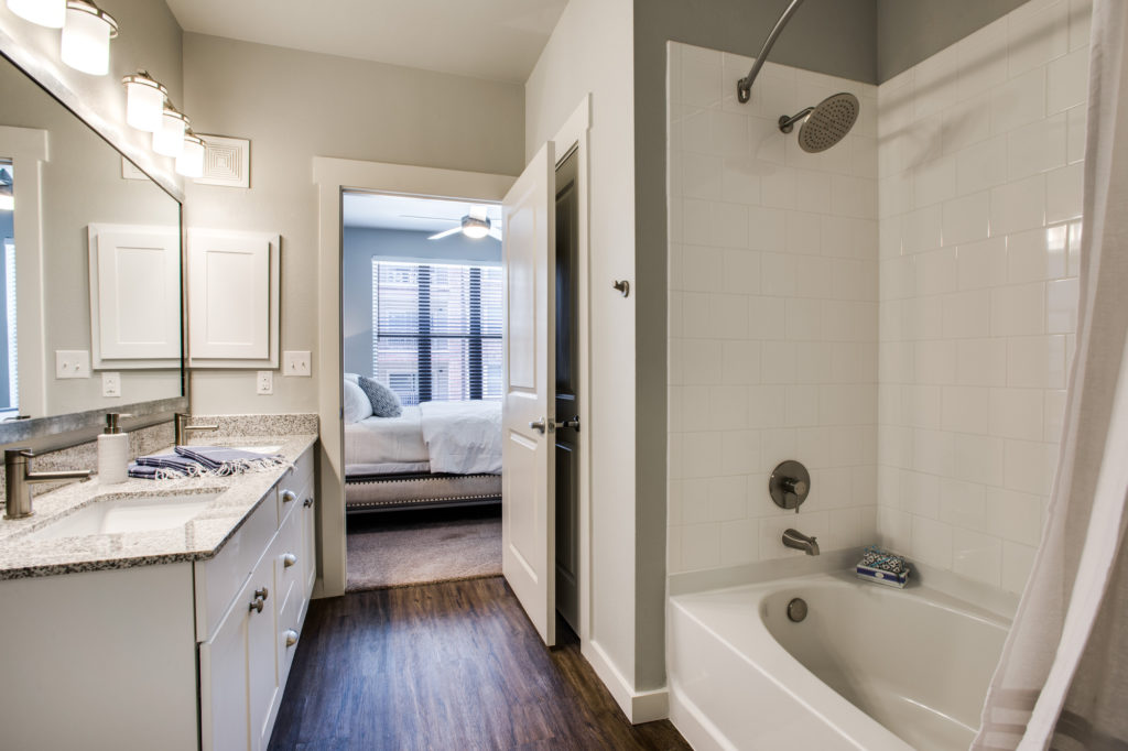 Model apartment bathrooms with double vanity, granite countertop, and tub-shower combination