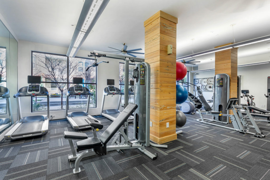 Fitness center interior with treadmills, weight benches, stair stepper, and medicine balls with large windows looking out towards the pool area.