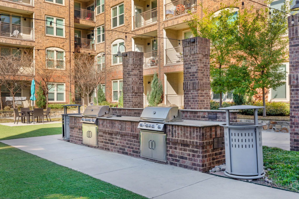 Set of outdoor stainless steel grills with countertop prep area and brick surrounds.
