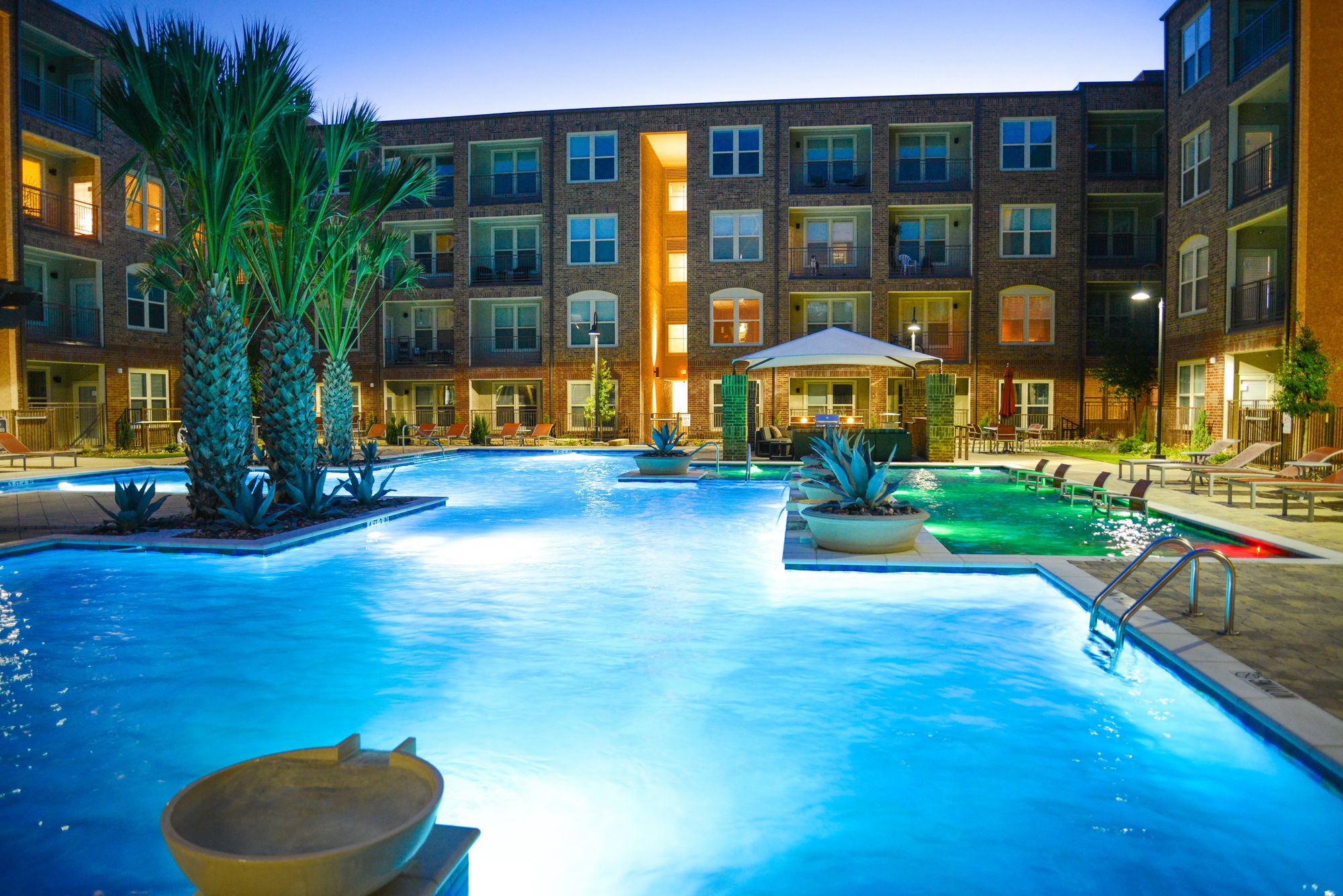 Resort-style pool with colorful accent lighting and palm trees